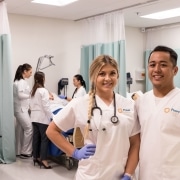 Two smiling nursing students wearing scrubs posing in a classroom