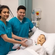 Nursing students smiling standing over a manikin in a hospital bed