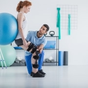 Woman with orthopedic problem exercising with ball while physiotherapist supporting her