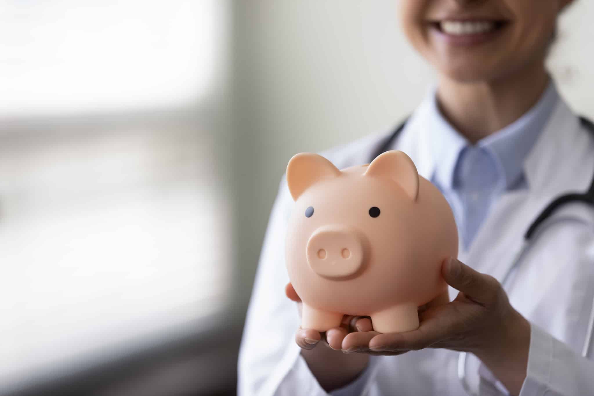 Close up of medical professional holding a piggy bank