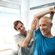 Older man smiling and lifting hand weights in physical therapy