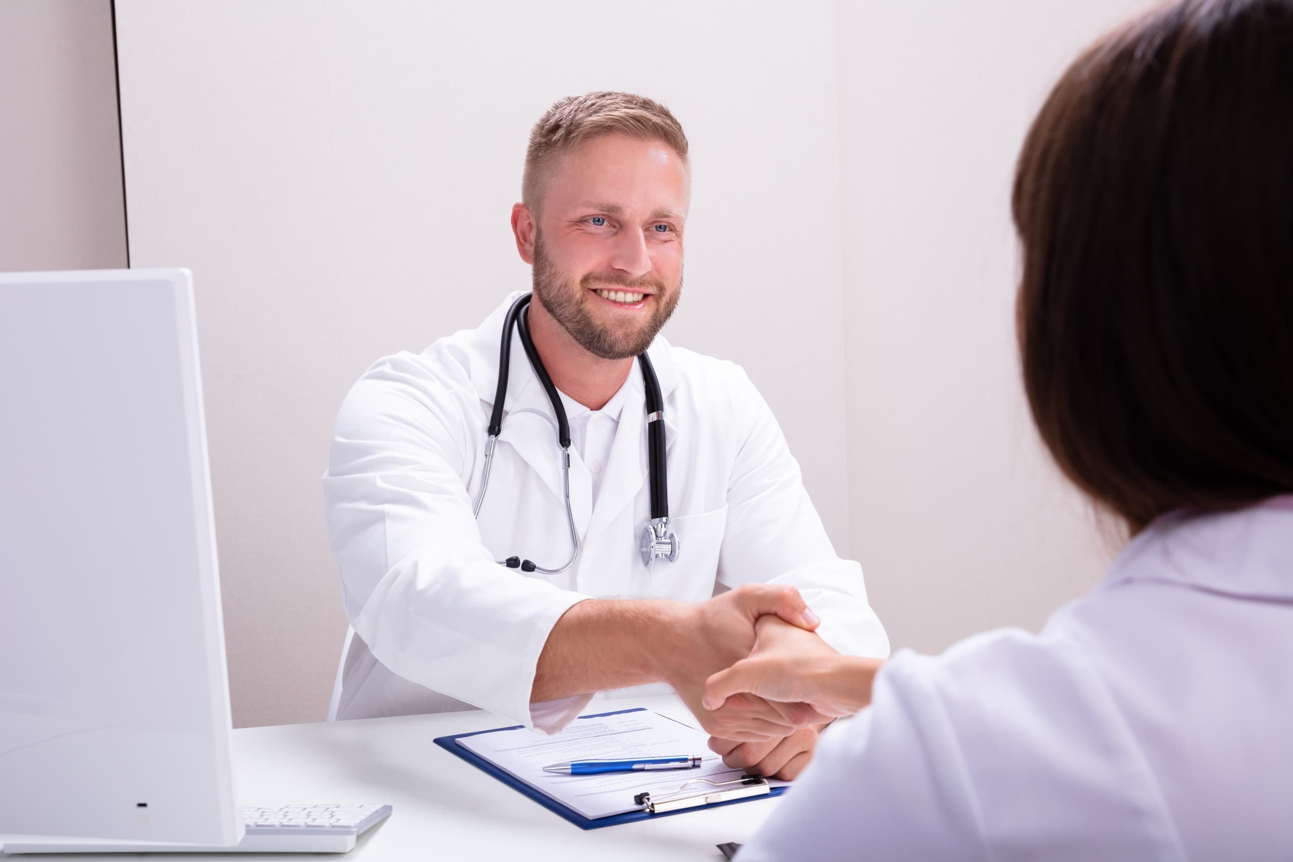 Male medical professional shaking hands with a woman at a desk